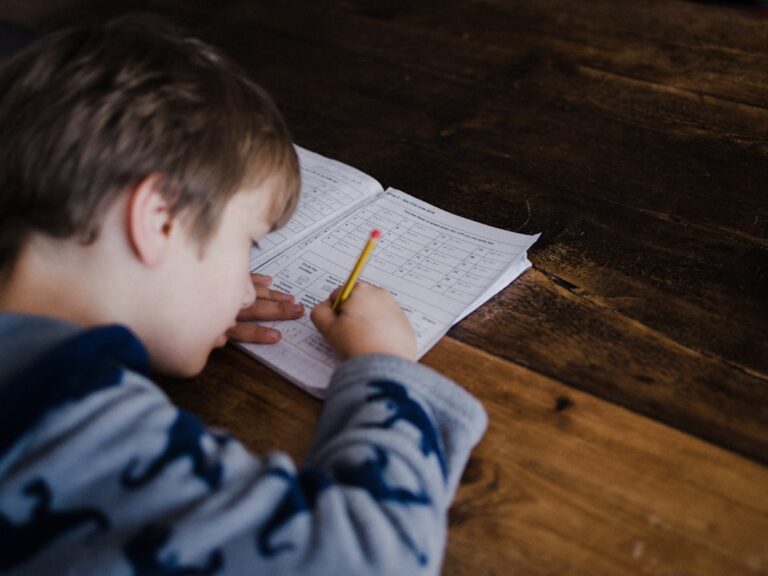 A child and parent reading together at a kitchen table with school books and papers scattered around.