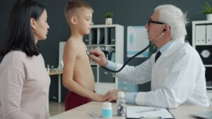 A pediatrician measuring the height of a young child in a bright, welcoming clinic exam room.