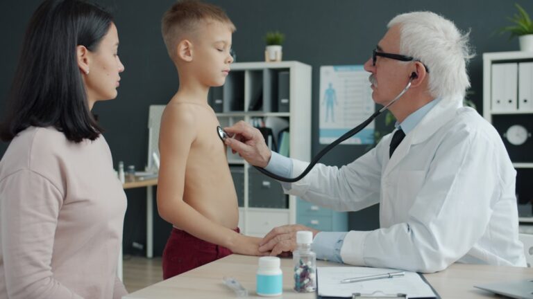 A pediatrician measuring the height of a young child in a bright, welcoming clinic exam room.